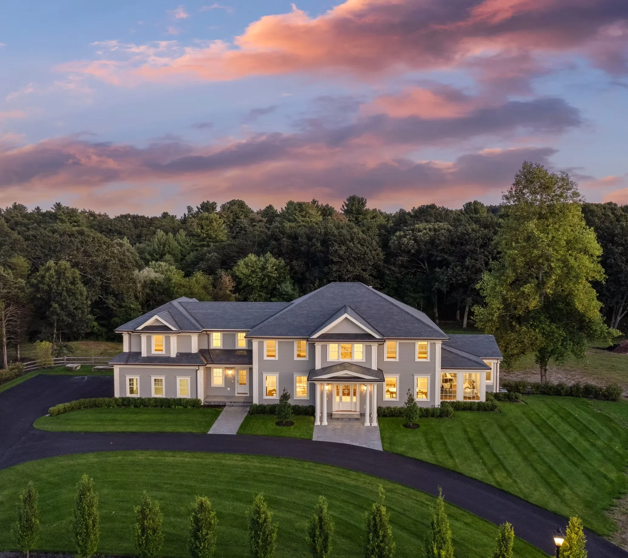 Two-story home with gray siding, white trim, dark roof, and curved driveway at dusk