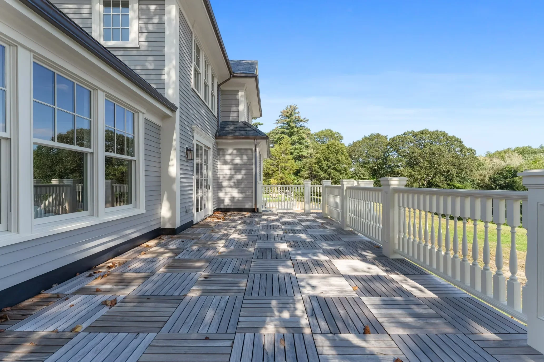 Composite deck with geometric pattern, white vinyl railings, and updated home exterior with large windows