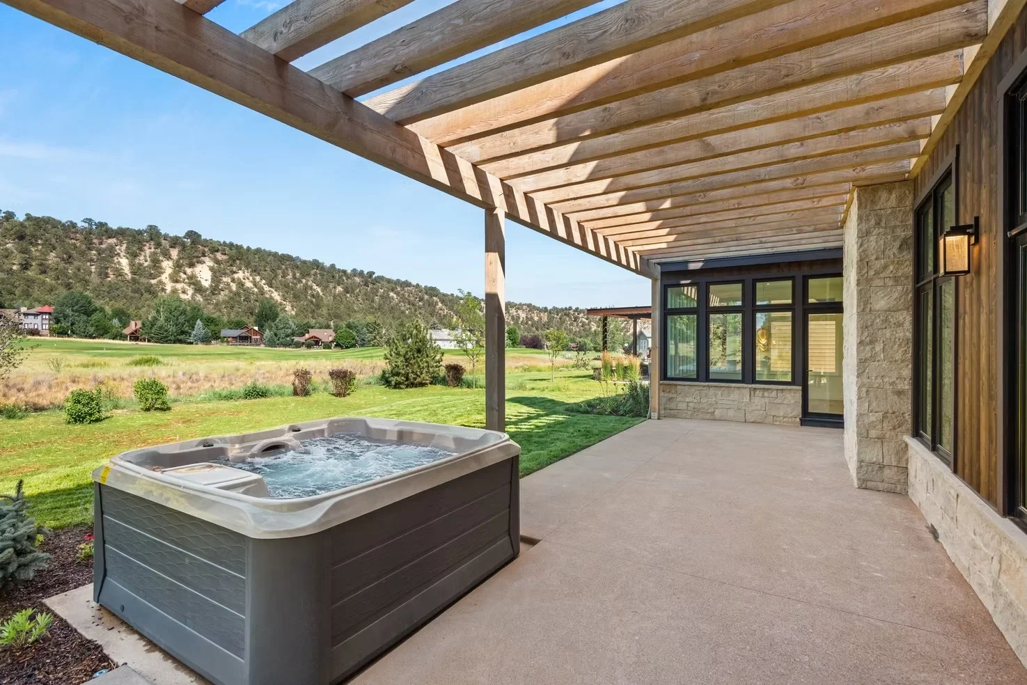 Timber pergola over stamped concrete patio with hot tub and stone-clad home exterior