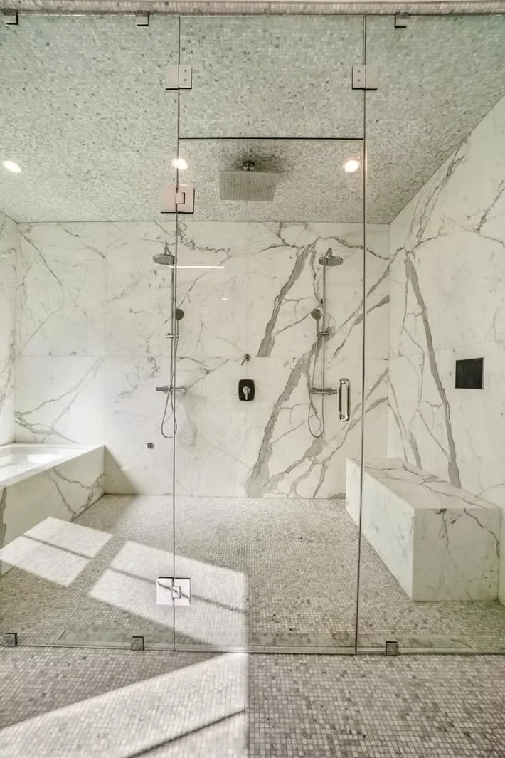 Luxury bathroom with marble shower walls, frameless glass enclosure, dual showerheads, and mosaic tile flooring
