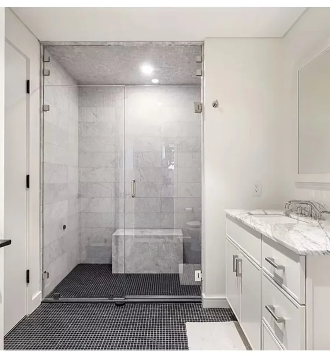 Master bathroom with marble tile shower, frameless glass doors, white vanity, and dark tile flooring