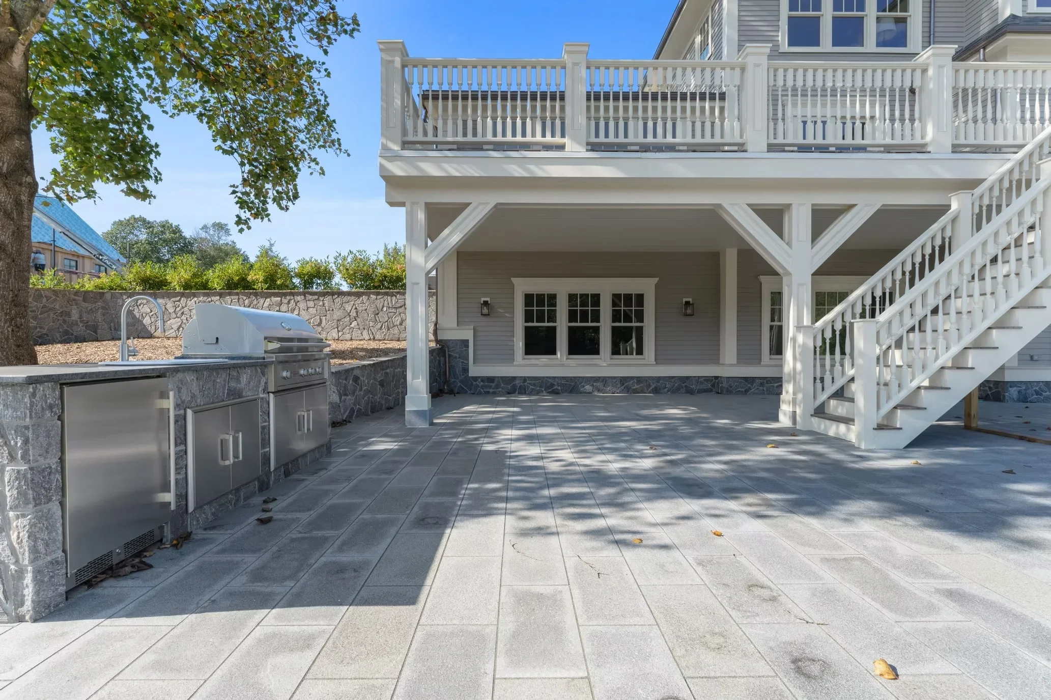 Covered patio with stone outdoor kitchen, stamped concrete flooring, white columns, and upper deck
