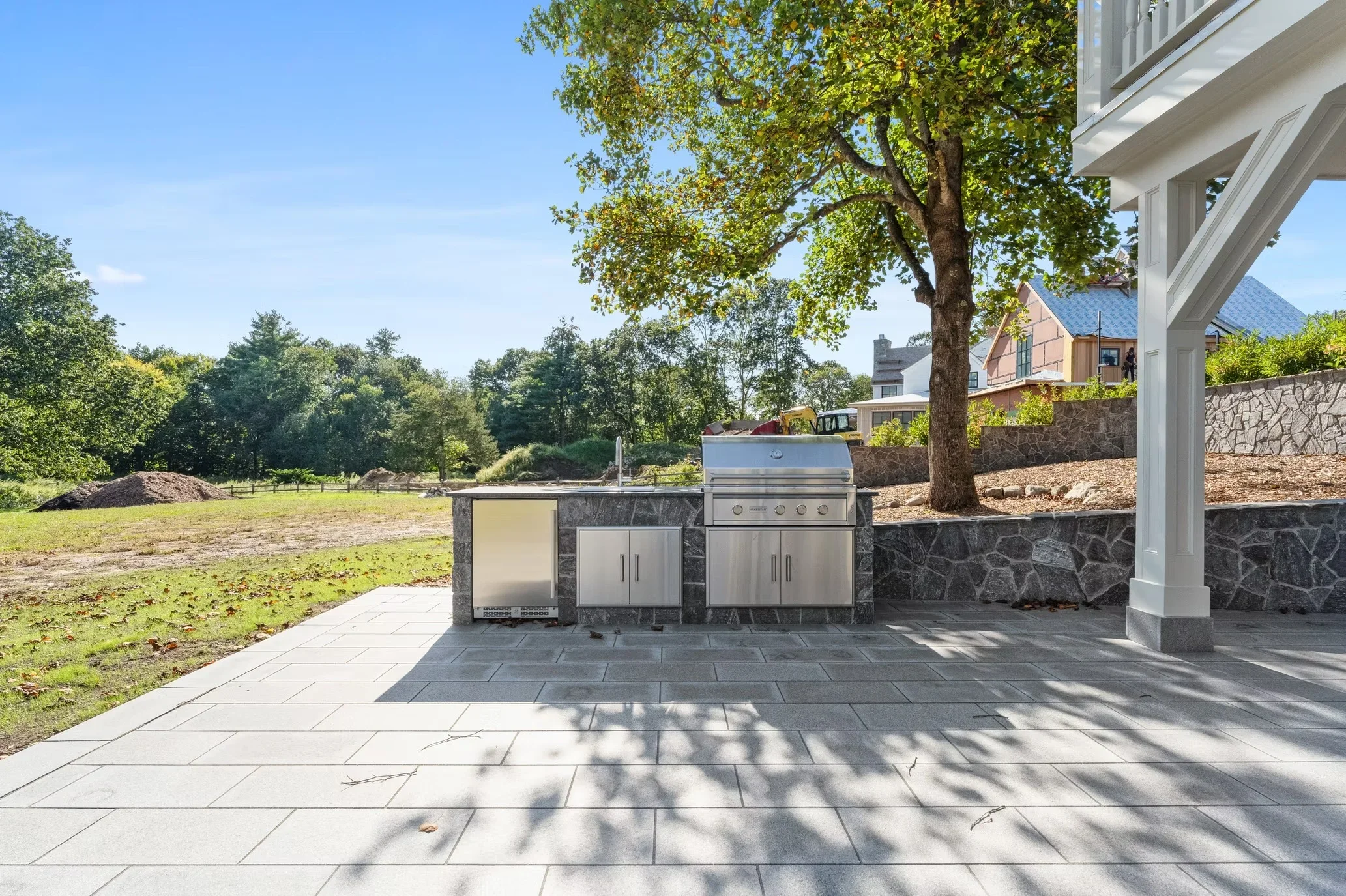 Stainless steel outdoor kitchen with stone base and paver patio adjacent to home