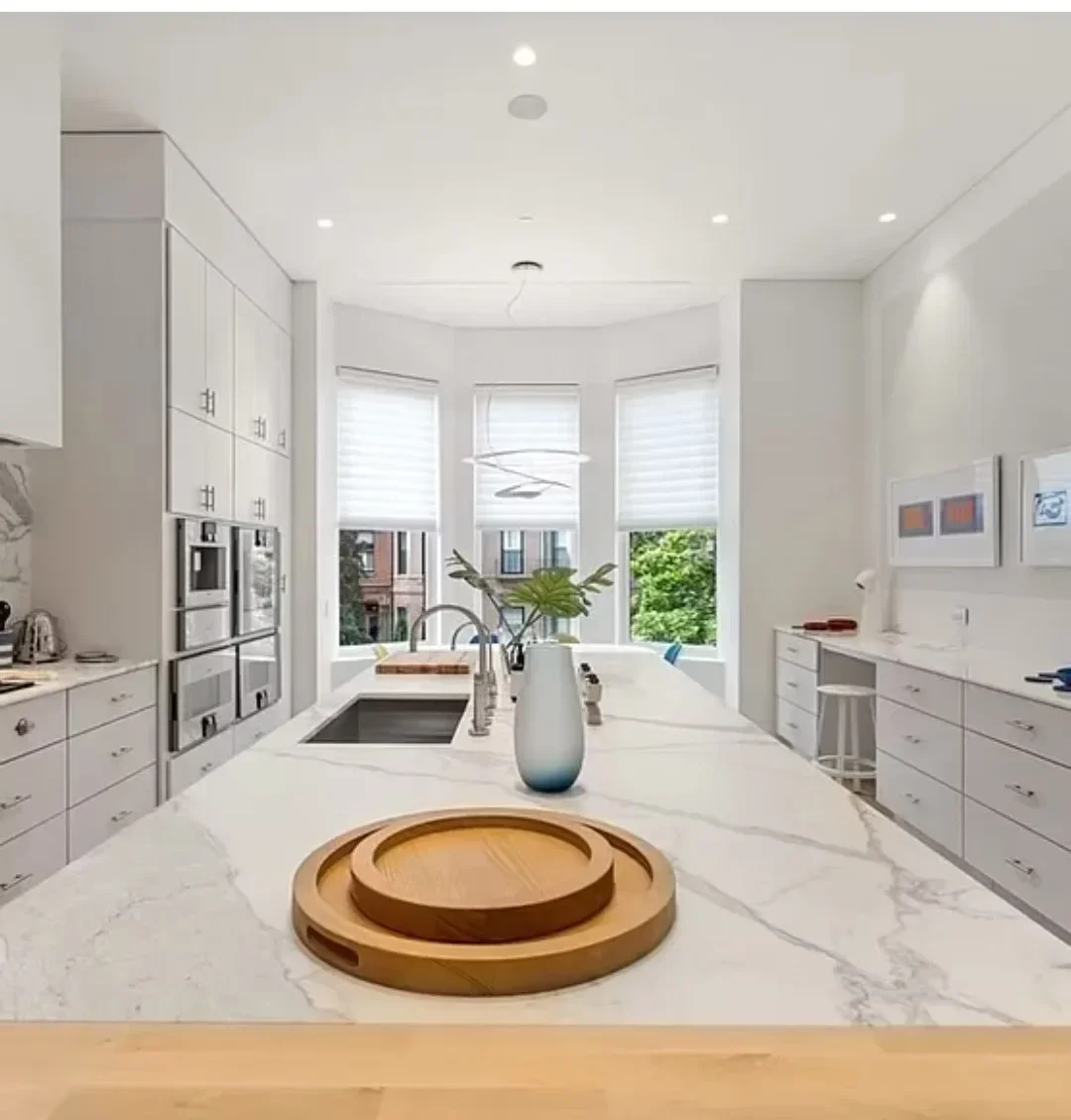 White kitchen with marble waterfall island, stainless steel appliances, and triple bay windows