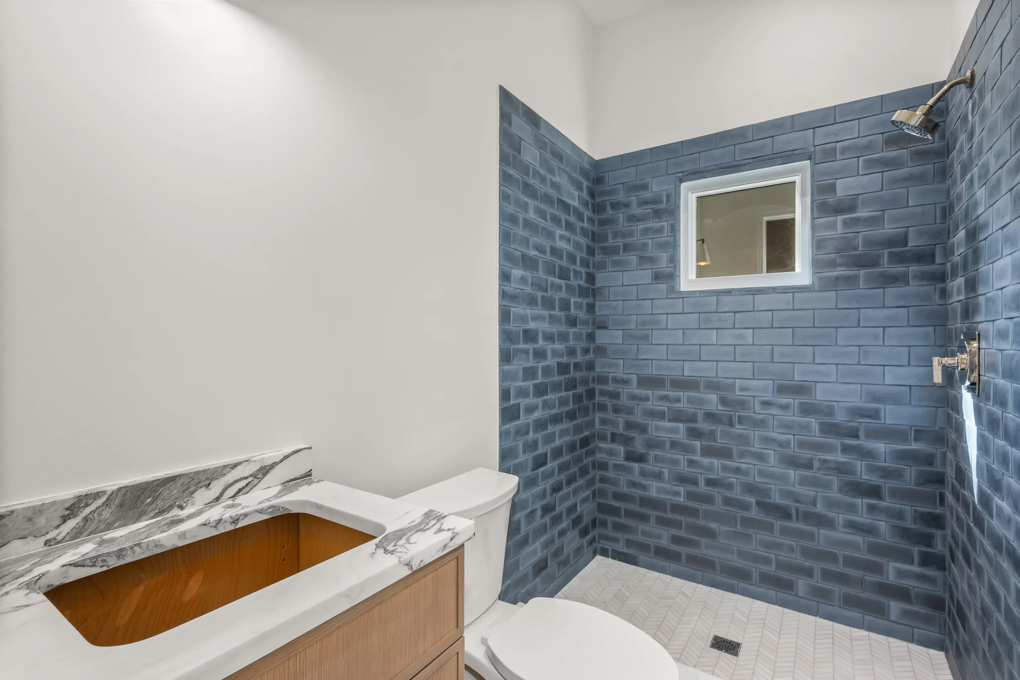 Blue subway tile shower with white tile floor, marble vanity, and framed mirror in renovated bathroom
