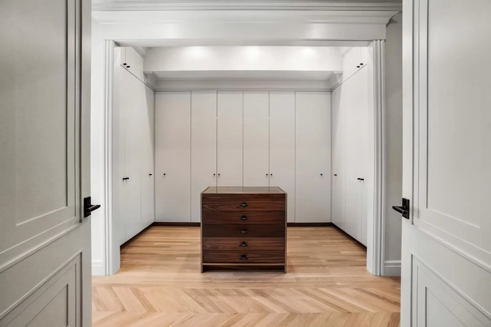 Walk-in closet with white built-in cabinetry, herringbone hardwood flooring, and recessed lighting