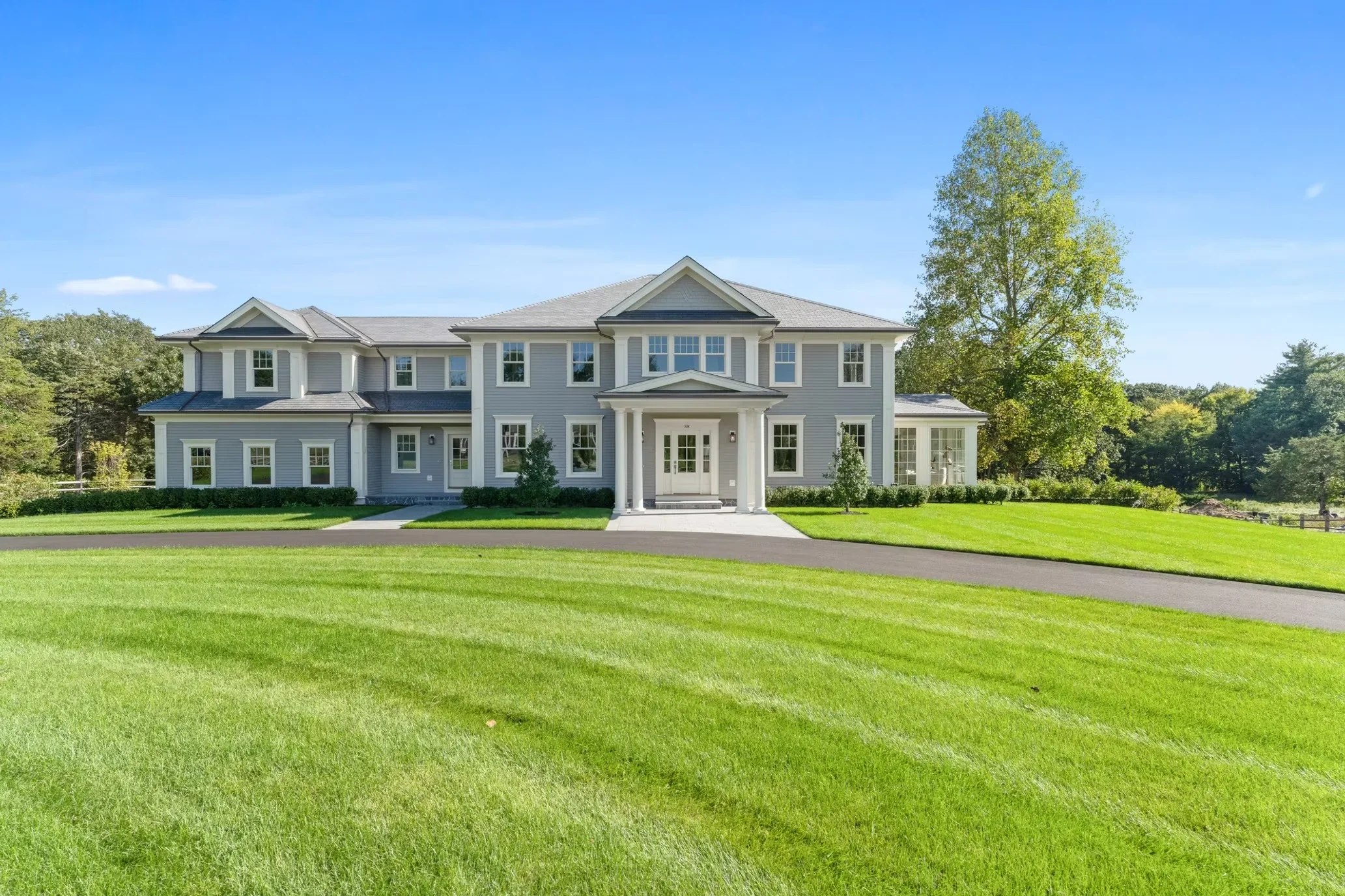 White colonial home with gabled rooflines, columns, and dark roof accents on manicured lawn
