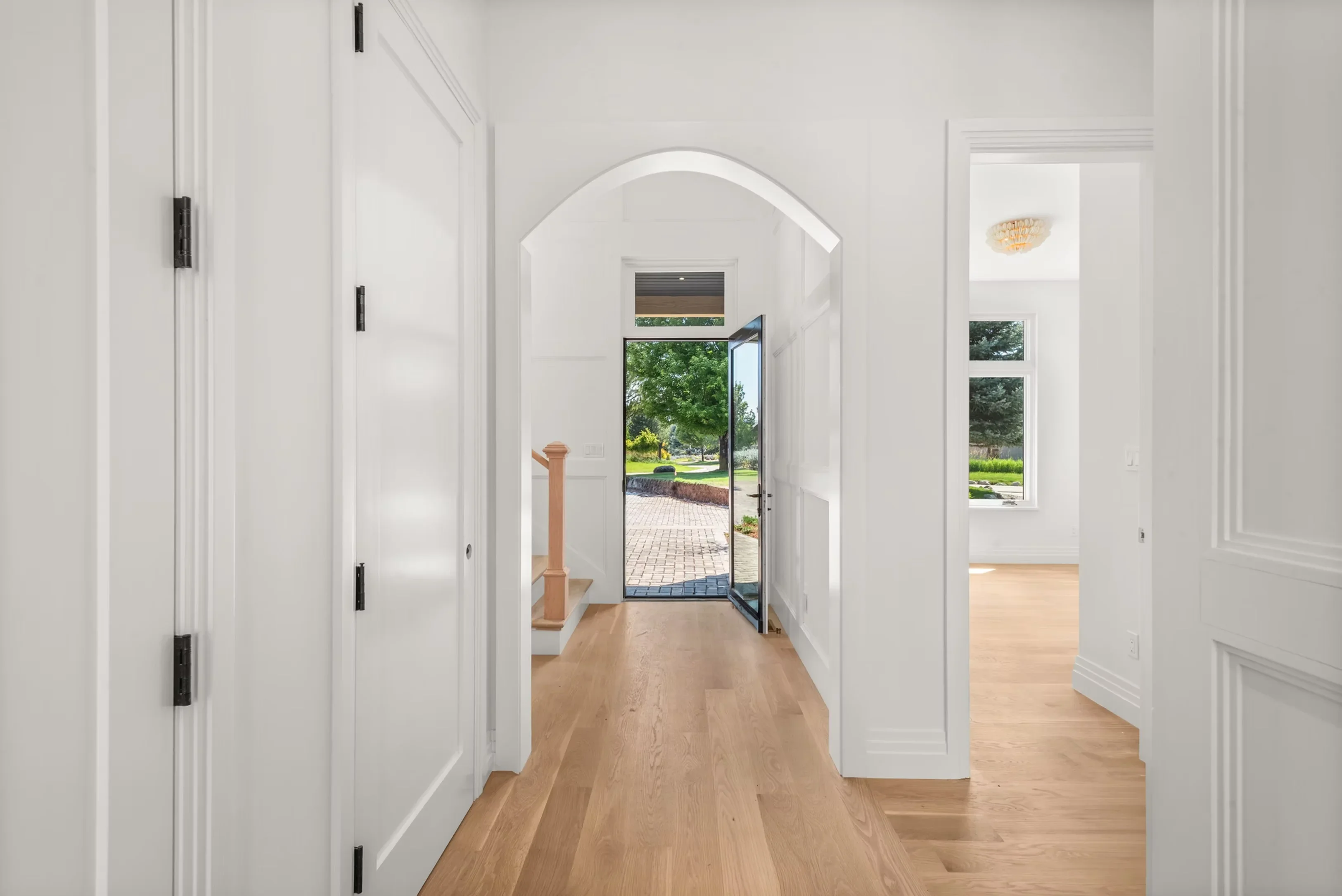 White hallway with arched doorway, hardwood floors, and glass doors opening to patio