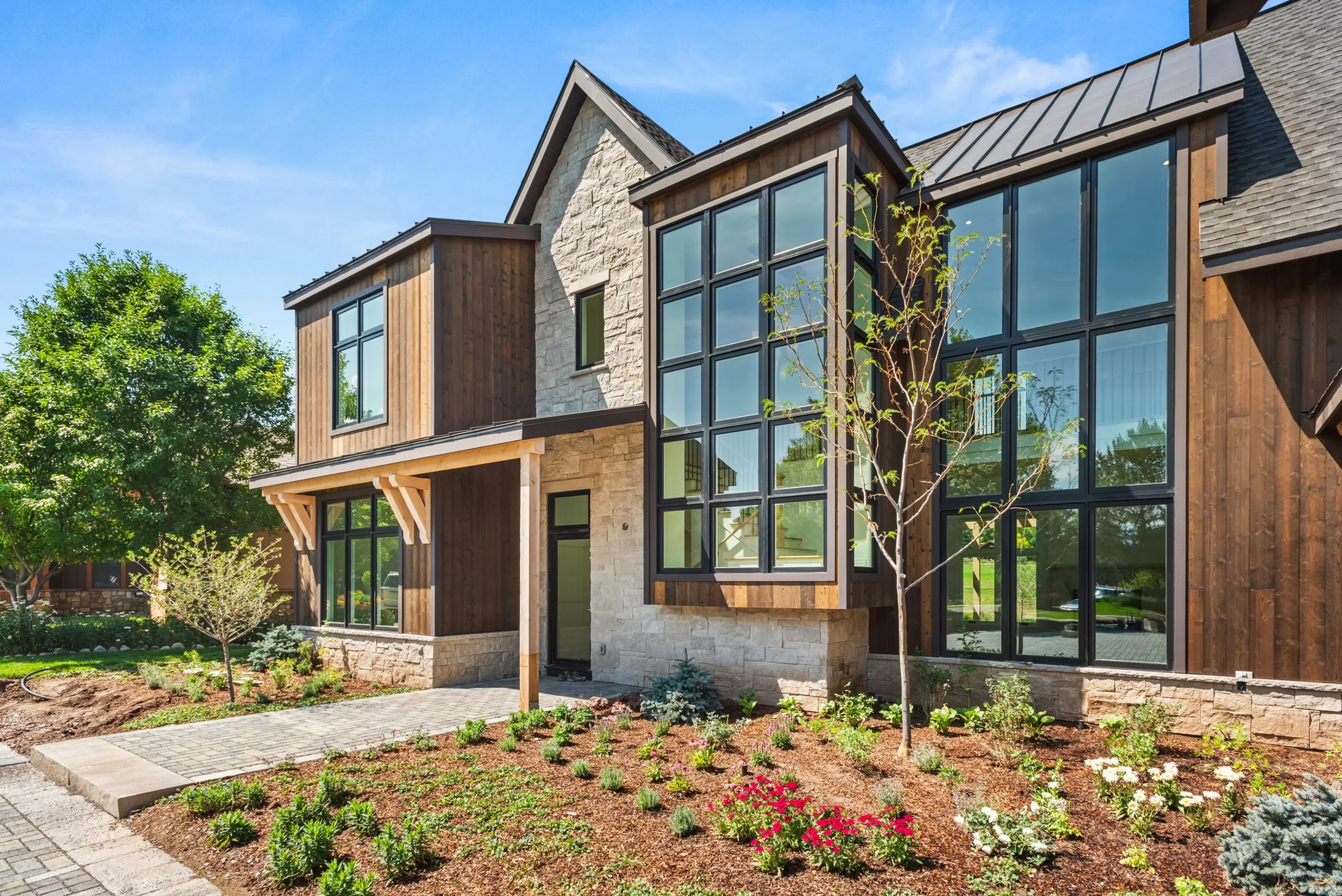 Modern farmhouse with stone and wood siding, black-framed windows, metal roof, and landscaped front yard