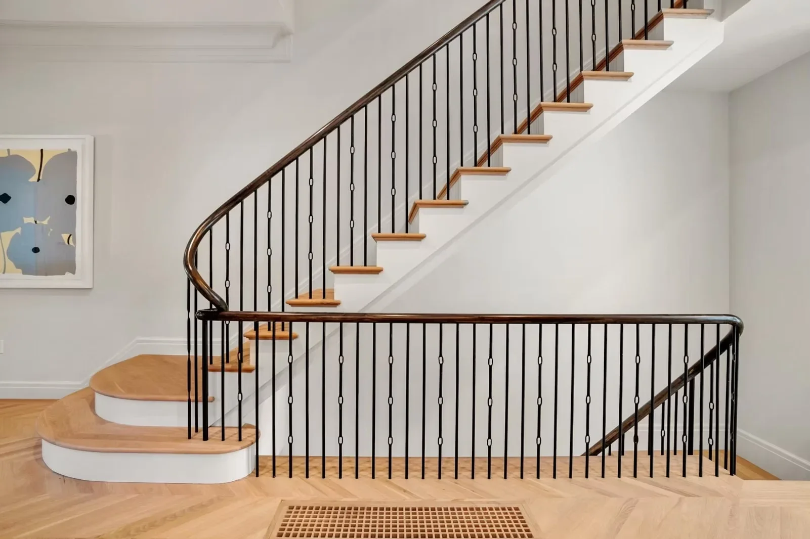 Curved wooden staircase with white risers and black metal vertical railing system