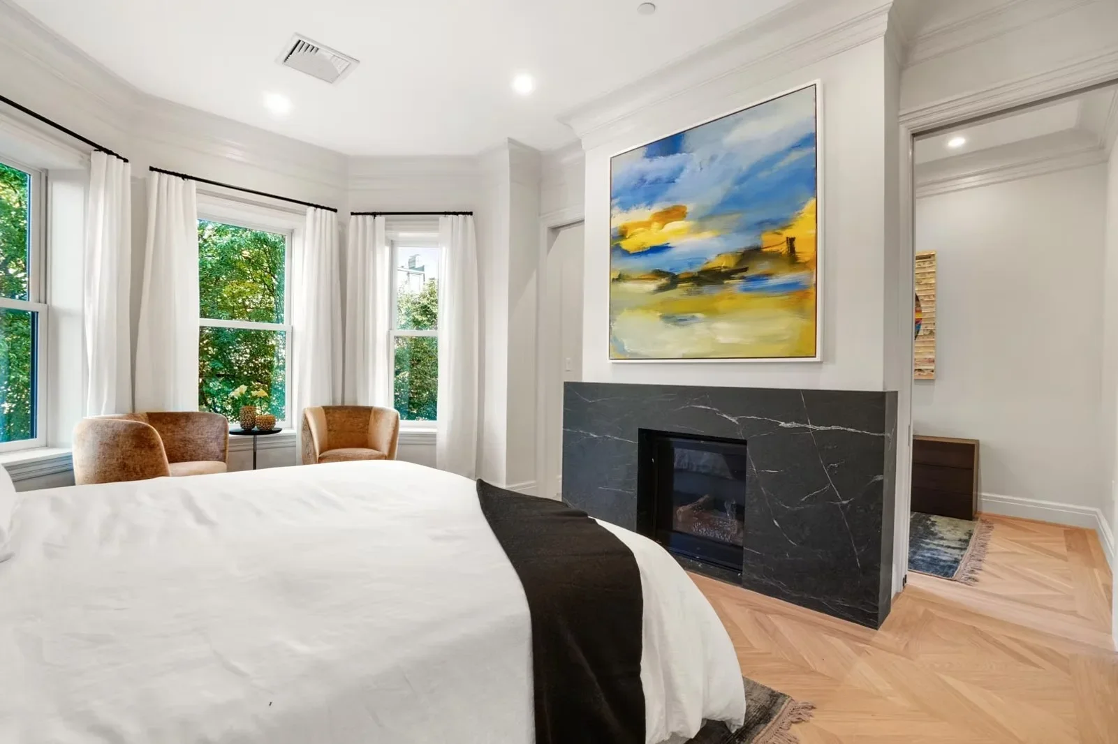Master bedroom with black marble fireplace, hardwood floors, and large windows with white curtains