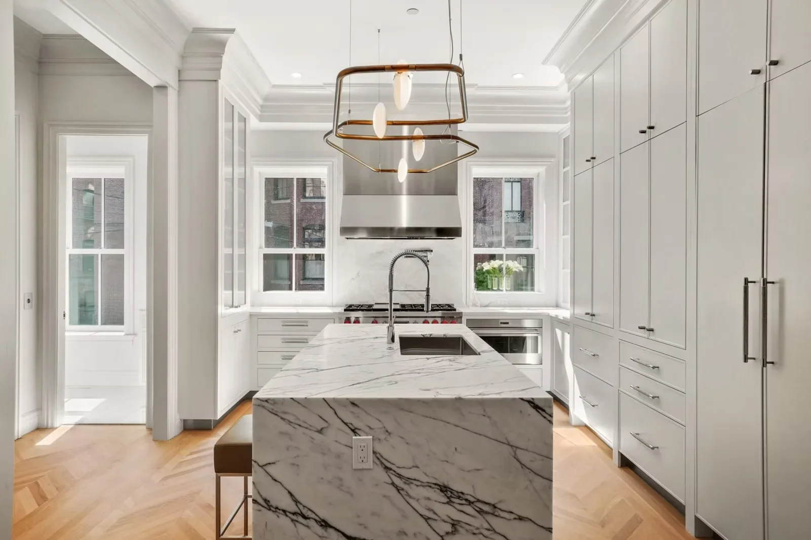 White kitchen with marble island, custom cabinetry, stainless steel appliances, and brass pendant lighting