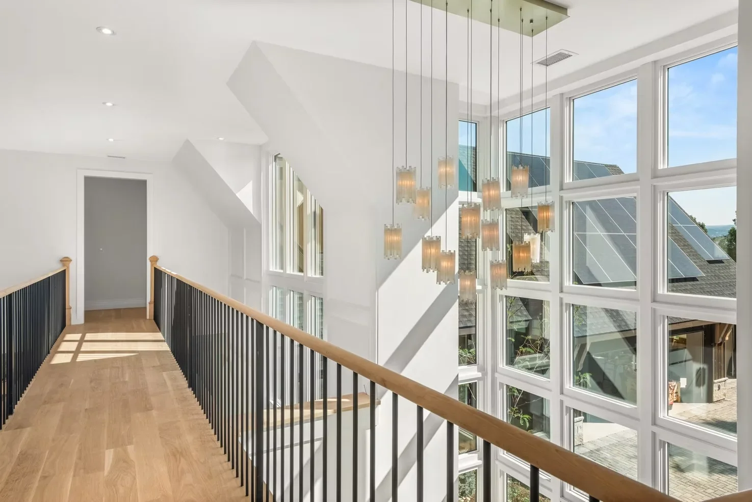 Two-story hallway with white drywall, wood flooring, black metal railing, and floor-to-ceiling glass walls