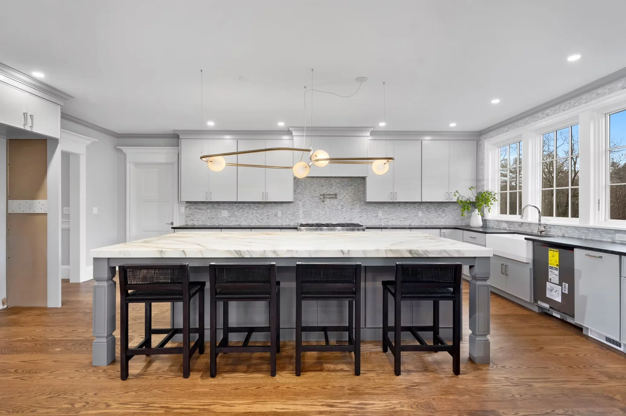 Modern kitchen with white cabinets, marble island, gray tile backsplash, and brass pendant lighting