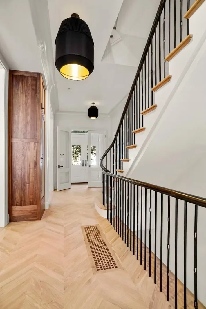Modern staircase with black metal balusters, oak handrails, herringbone wood flooring, and pendant lighting