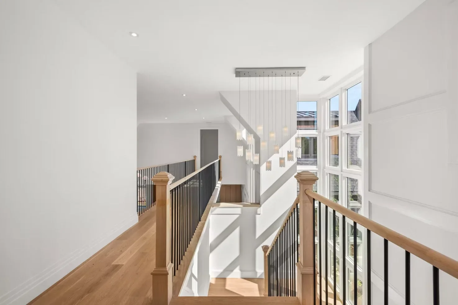 Upper hallway with wood railings, metal balusters, hardwood floors, and pendant lighting