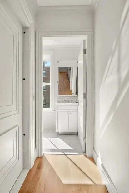 White painted hallway with custom bathroom vanity, crown molding, and hardwood flooring